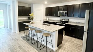 A modern kitchen with dark cabinets, a large island with bar stools, a stainless steel refrigerator, and a microwave. - Treasure Coast Retreat 3 bedroom duplex home (PORT ST LUCIE)