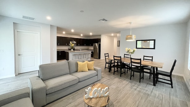 A modern living room with a grey sofa, a wooden coffee table, and a dining area with a wooden table and chairs. - Treasure Coast Retreat 3 bedroom duplex home (PORT ST LUCIE)