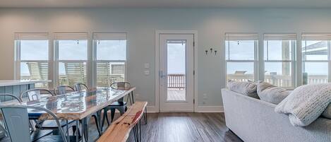 Amplia habitación con una gran mesa de madera para comer, varias sillas, un sofá y una puerta que da a un balcón exterior.