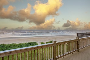 Eine Holzterrasse mit Blick auf einen Strand und den Ozean, am Himmel ziehen Wolken vorbei.