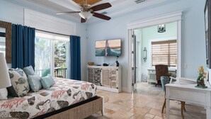 A bedroom with a bed, a desk, a chair, a ceiling fan, a TV, and a window with curtains.