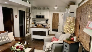 A cozy living room with a fireplace, a dining area with a kitchen in the background, and a Christmas tree.