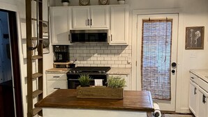 A kitchen with white cabinets, a wooden island, a microwave, and a hanging light fixture.