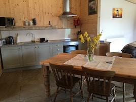 Une cuisine chaleureuse avec des meubles en bois, une table à manger entourée de chaises, un vase rempli de fleurs et un tableau accroché au mur.