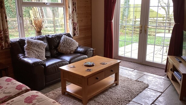 Un salon chaleureux avec un canapé en cuir, une table basse en bois et une vue sur l’extérieur grâce à de grandes portes vitrées.