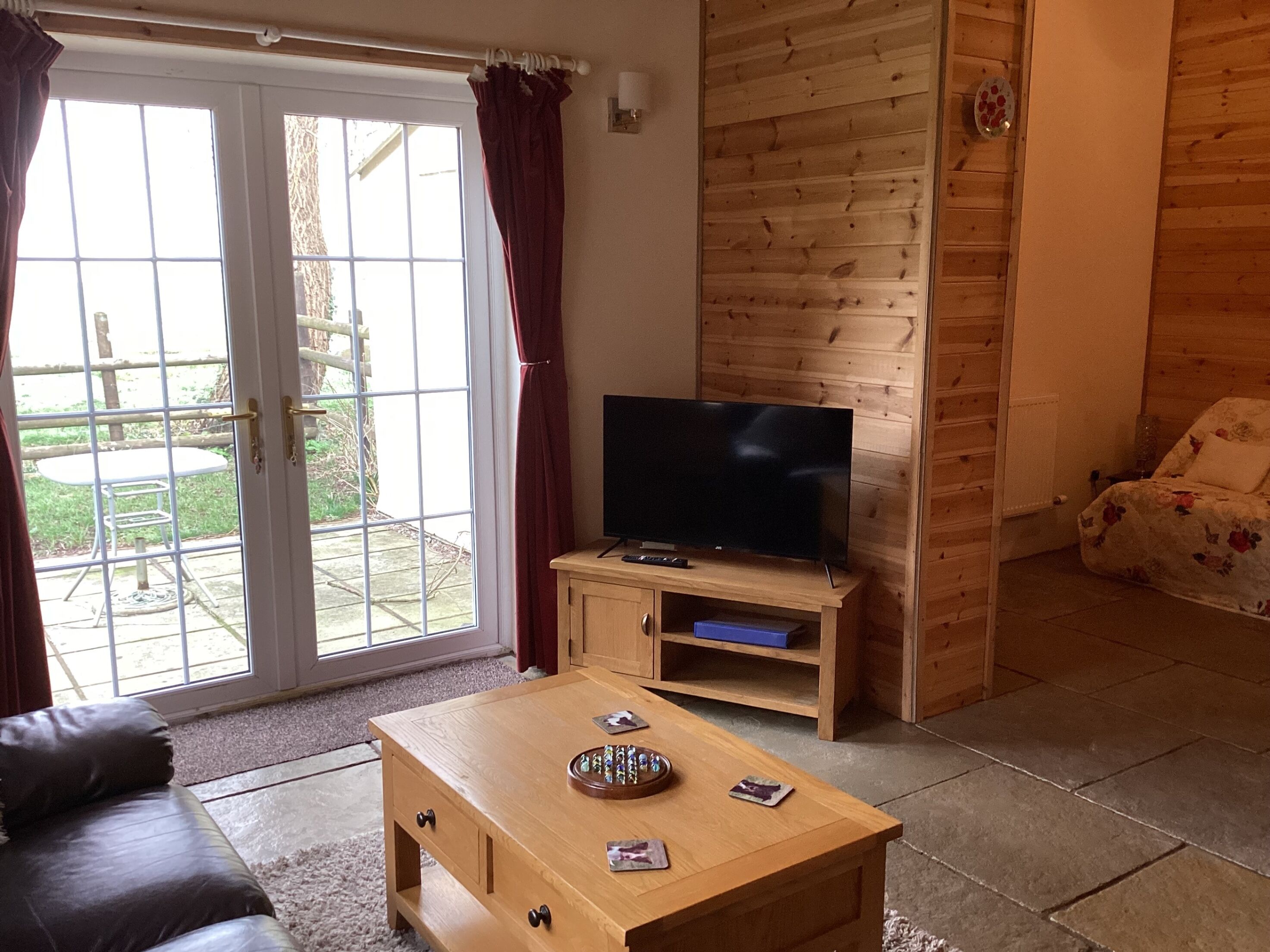 Een woonkamer met een televisie op een houten dressoir, een bank, een salontafel met spullen erop en een schuifdeur naar buiten.