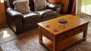 Un salon chaleureux avec un canapé en cuir marron, des coussins moelleux, une table basse en bois et une vue sur la verdure grâce à de grandes fenêtres.