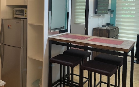 A compact kitchen with a refrigerator, a microwave, and a small dining table with stools.