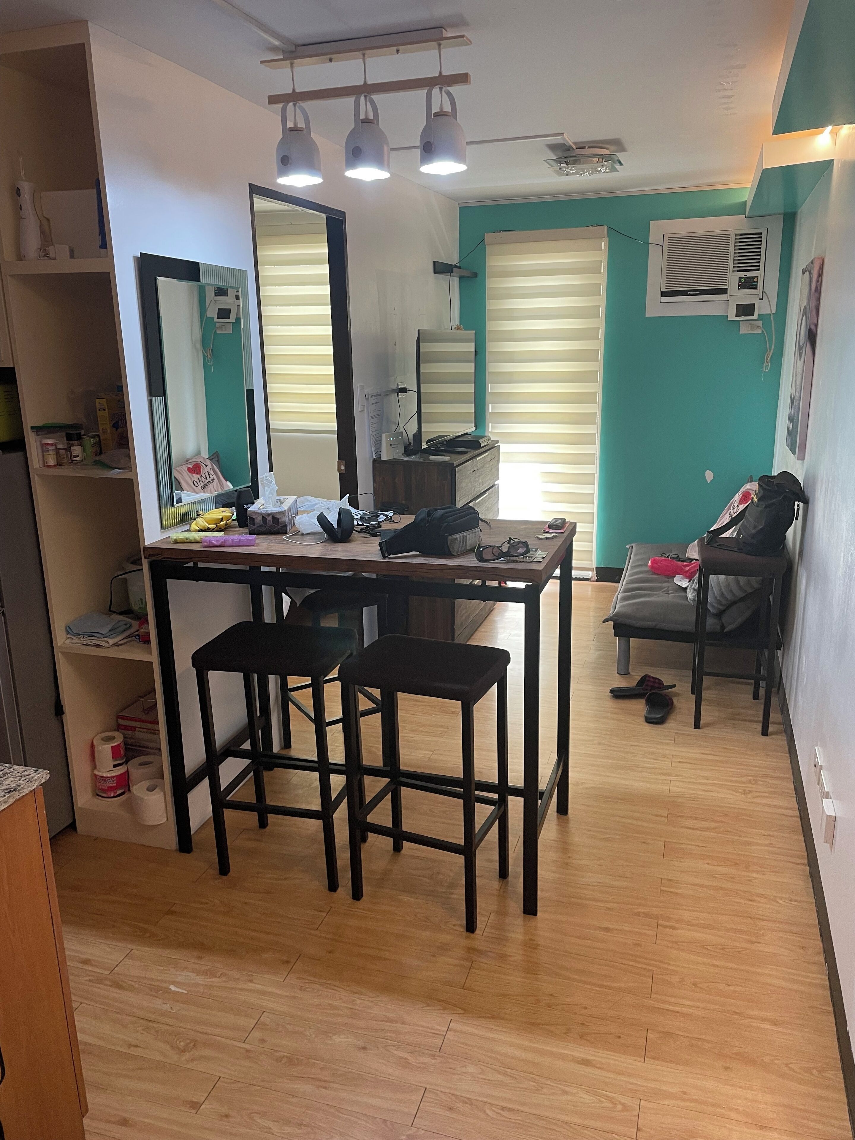 Een ruimtelijk ingerichte leefruimte met kitchenette, een eethoek met twee krukken, een bank en een kleine tafel.