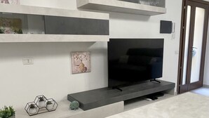 Una sala de estar moderna con un televisor de pantalla plana, estanterías empotradas y un frutero de vidrio sobre la encimera.