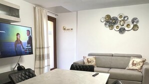 Una sala de estar moderna con un televisor de pantalla plana, un sofá gris y una mesa de comedor con sillas.