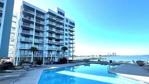 A modern hotel with a pool, multiple balconies, and a view of the sea.