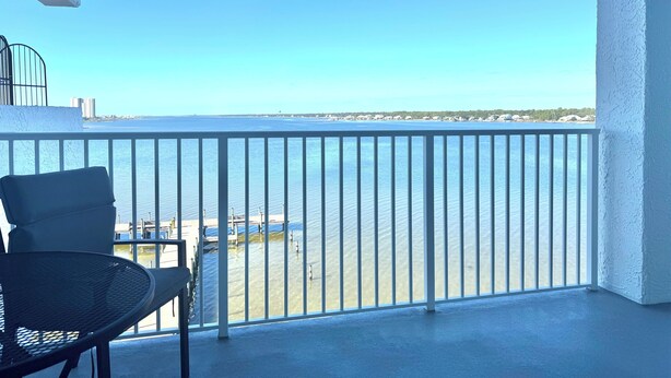 A balcony with a view of the sea, a chair, and a table.