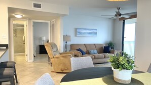 A modern living room with a beige sofa, a tan armchair, and a dining table with a plant centerpiece.