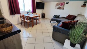 Un salon confortable avec un coin repas, un téléviseur à écran plat fixé au mur et une grande fenêtre agrémentée de rideaux.