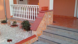 Une entrée d’immeuble avec une balustrade blanche, des marches menant à une porte et des plantes en pot.