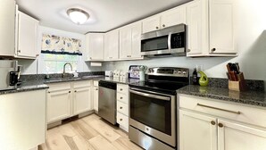 Una cocina con armarios blancos, microondas, cafetera y lavavajillas.