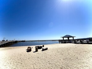 Ein Strand mit einer Holzstege, einem Pavillon und Baumstämmen im Sand.