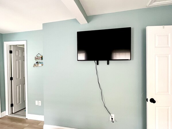 A room with a mounted TV on a light blue wall, a white door, and a small welcome sign.
