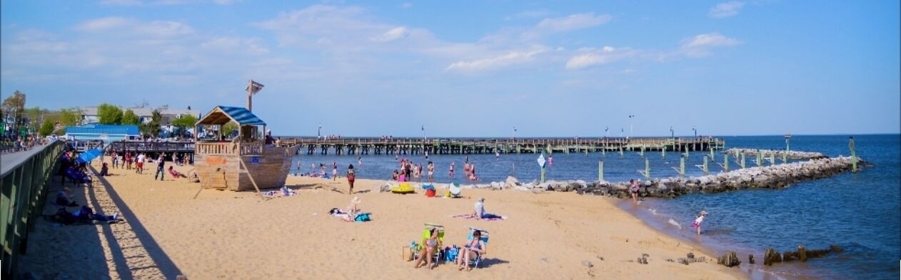Een strand met een pier die zich uitstrekt in het water, mensen ontspannen op het zand en een badwachter uitkijktoren.