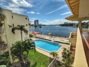 A swimming pool with a view of the water, a balcony with a railing, and a building with a satellite dish.