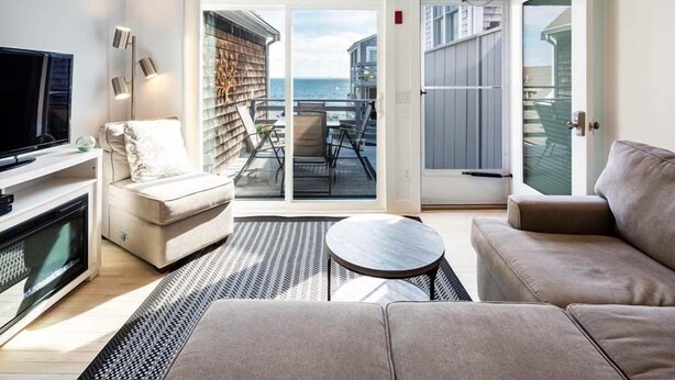 Sala de estar moderna com televisão, sofá e vista para o mar através de uma porta de vidro deslizante.