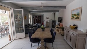 A spacious dining area with a long table and chairs, a kitchen with cabinets and a refrigerator, and a living area with a sofa and a fireplace. - Villa with pool at the foot of the Luberon (Maubec)