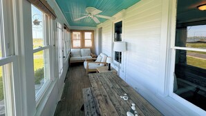 Eine überdachte Veranda mit Deckenventilator, Holzbanken und einer Couch.