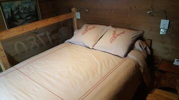Ein Bett mit Holz-Kopfteil, zwei mit Hirsch-Motiv versehene Kissen und ein Nachttisch mit Lampe.