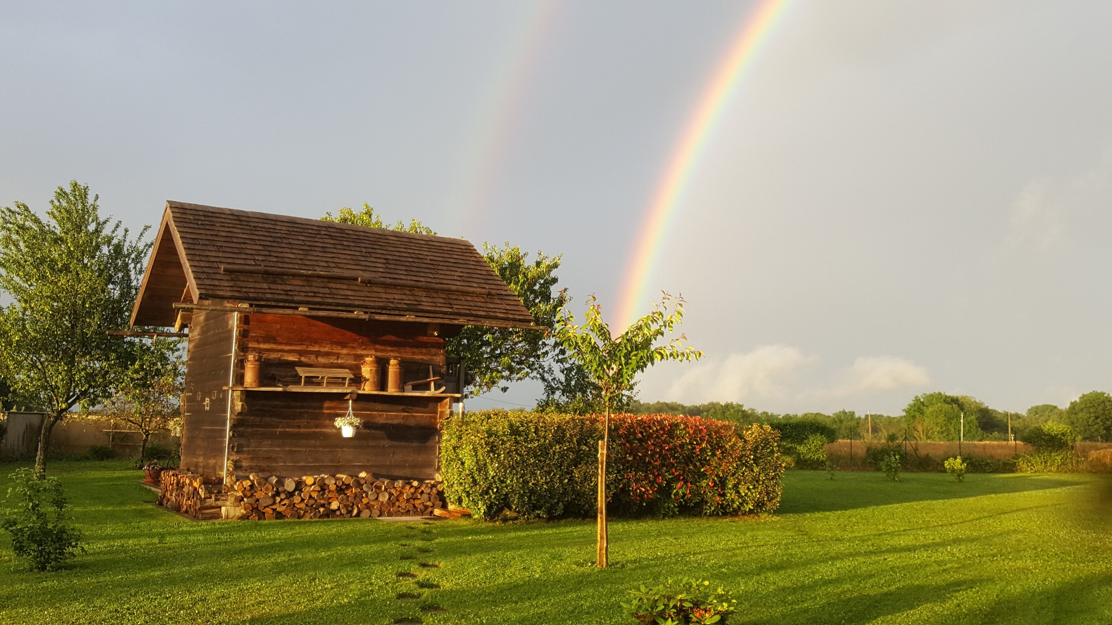 Un rustico chalet in legno con tetto spiovente, immerso in un prato curato e protetto da un siepe.