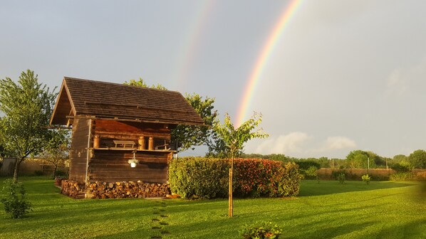 A rustic wooden cabin with a sloped roof, surrounded by a well-maintained lawn and a hedge.
