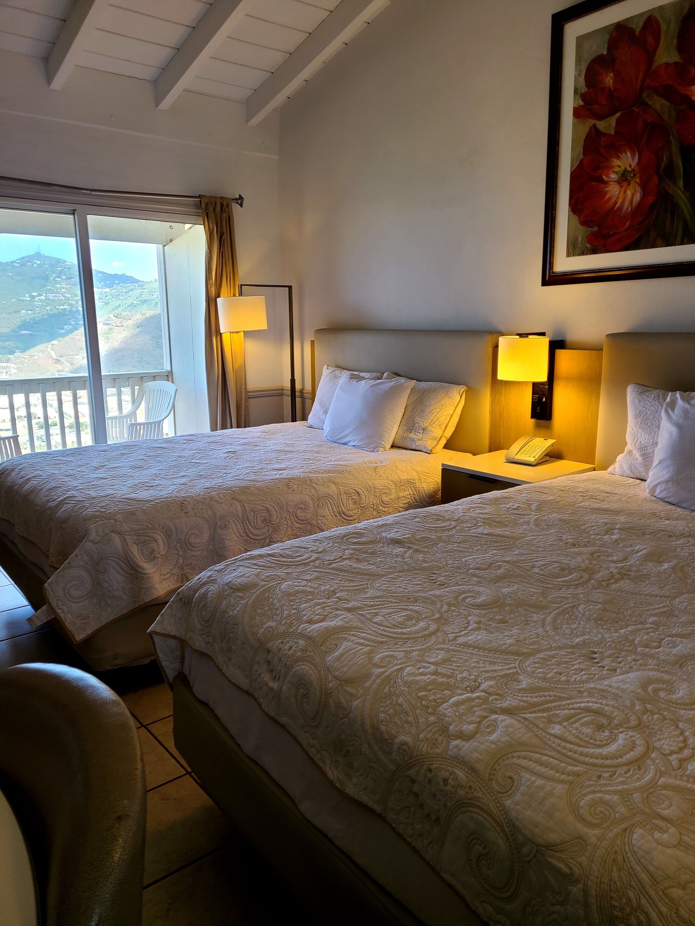 Een hotelkamer met twee bedden, een balkon en een bloemen schilderij.