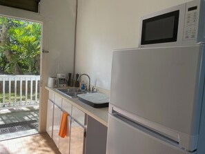 Eine Küche mit Kühlschrank, Mikrowelle, Spüle und einem Fenster mit Blick auf Grünflächen.