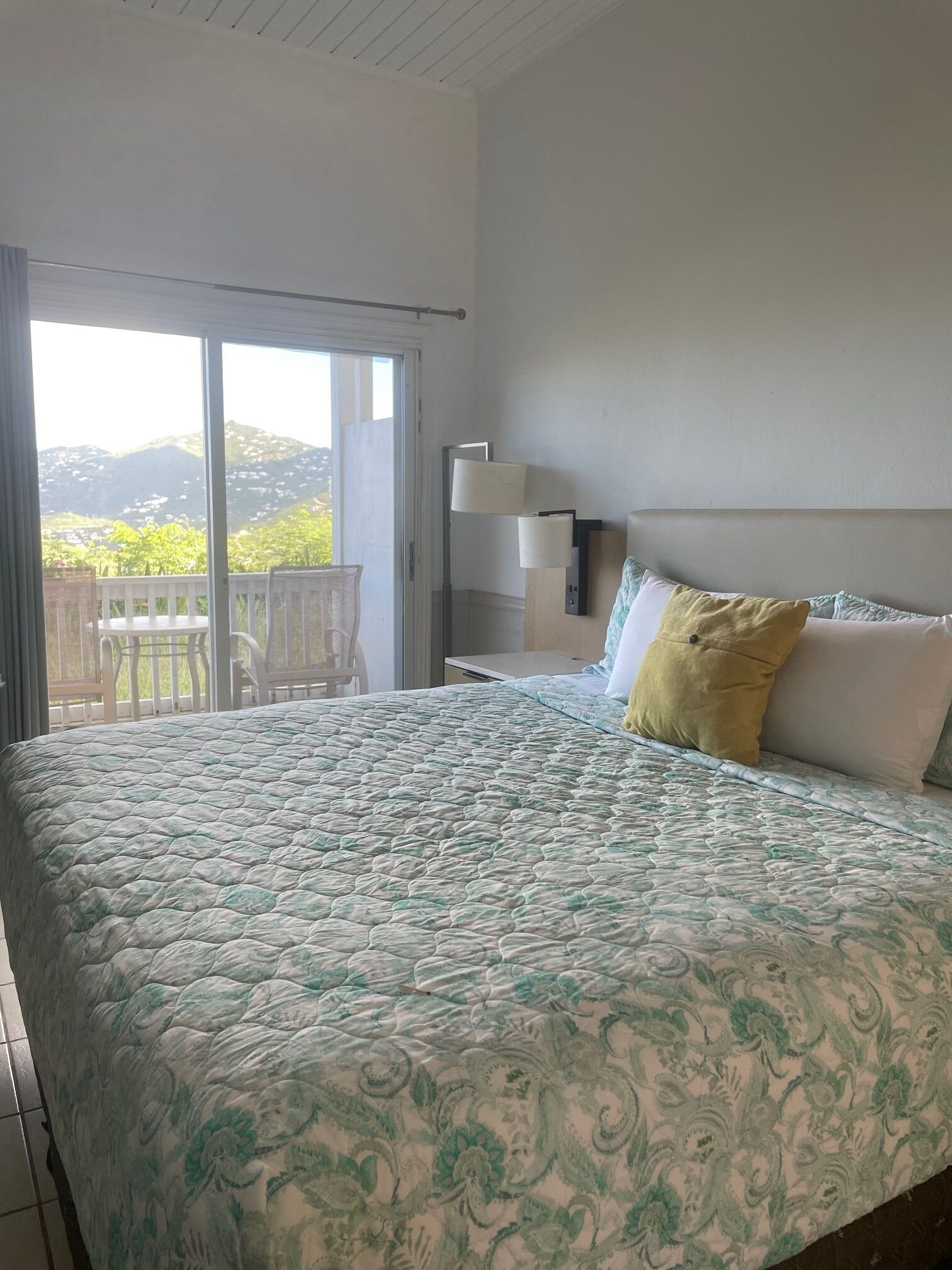 Un dormitorio con cama, una mesita de noche, una lámpara y vistas al exterior.