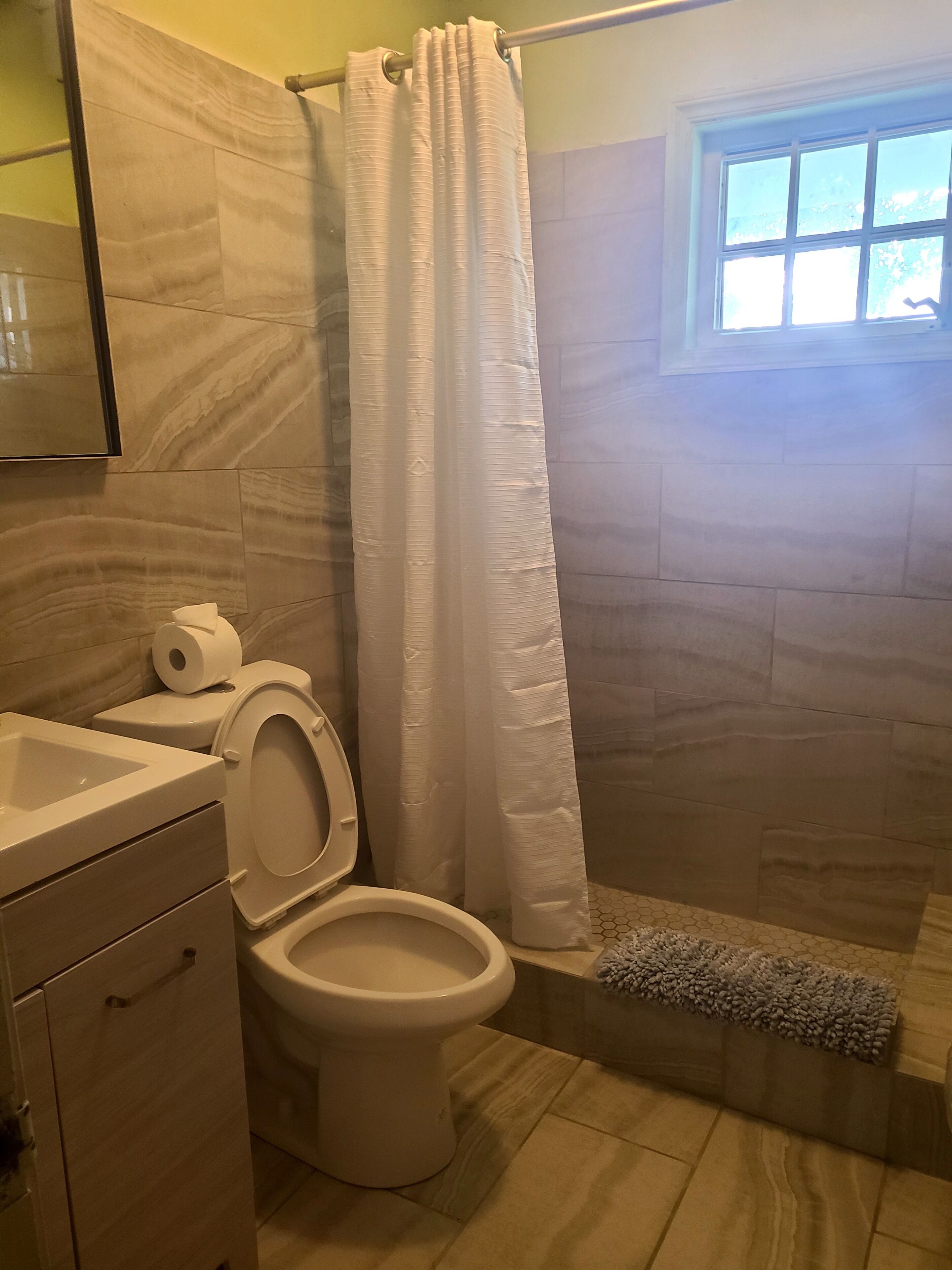 Un baño con inodoro, lavamanos, cortina de ducha y ventana.