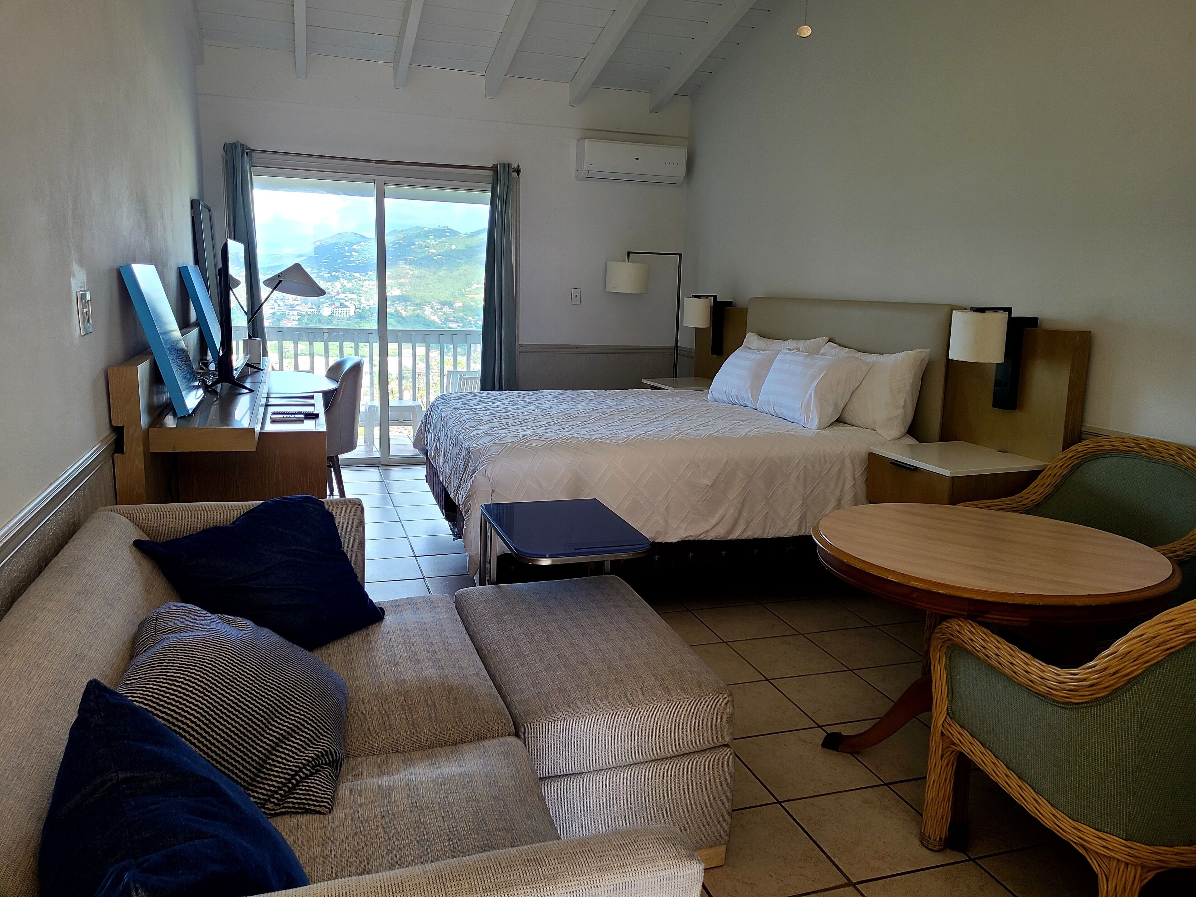 Een hotelkamer met twee bedden, een bank, een kleine tafel en een stoel. Er is een balkon met uitzicht op het landschap.
