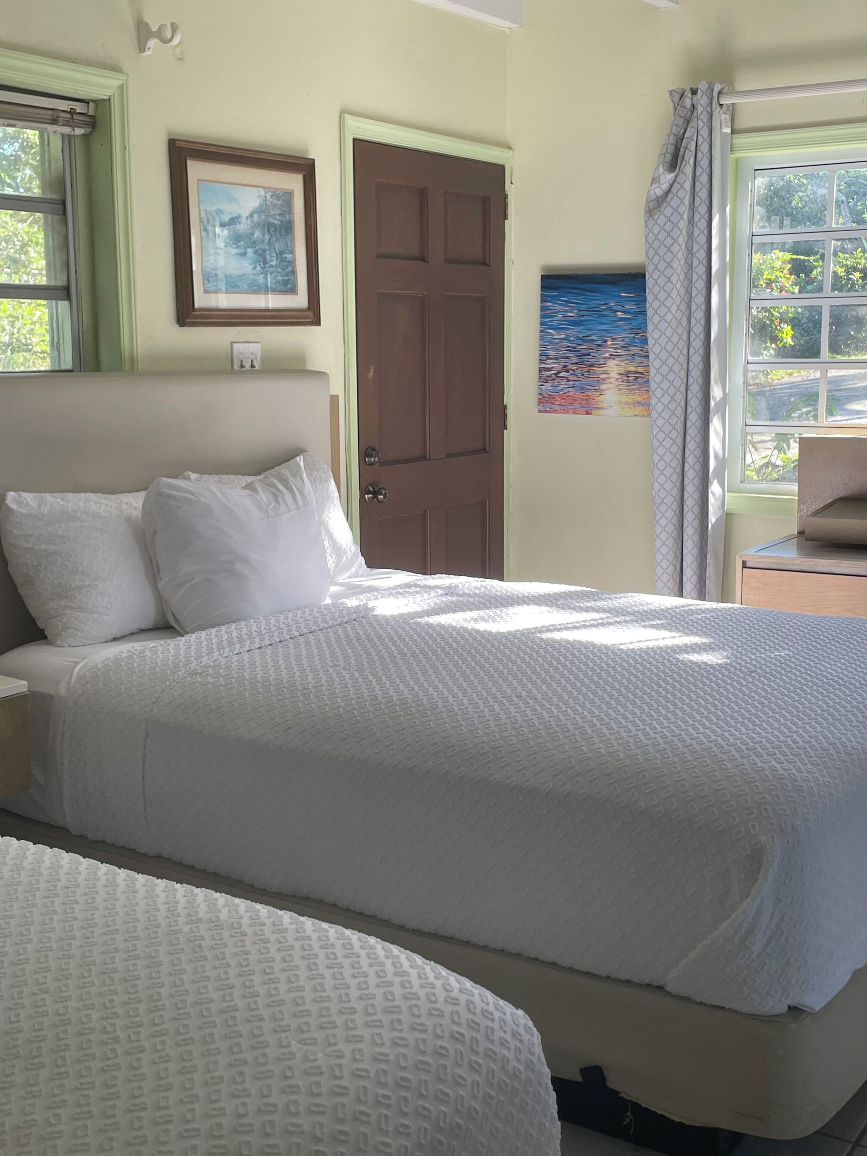 A bedroom with a bed, a door, a window with curtains, and a wall-mounted picture.