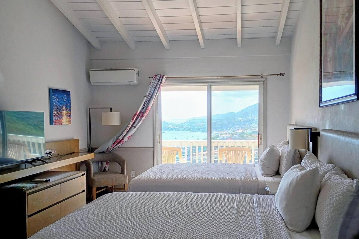 Un dormitorio con dos camas, un escritorio, una silla y una ventana con vistas al paisaje costero.