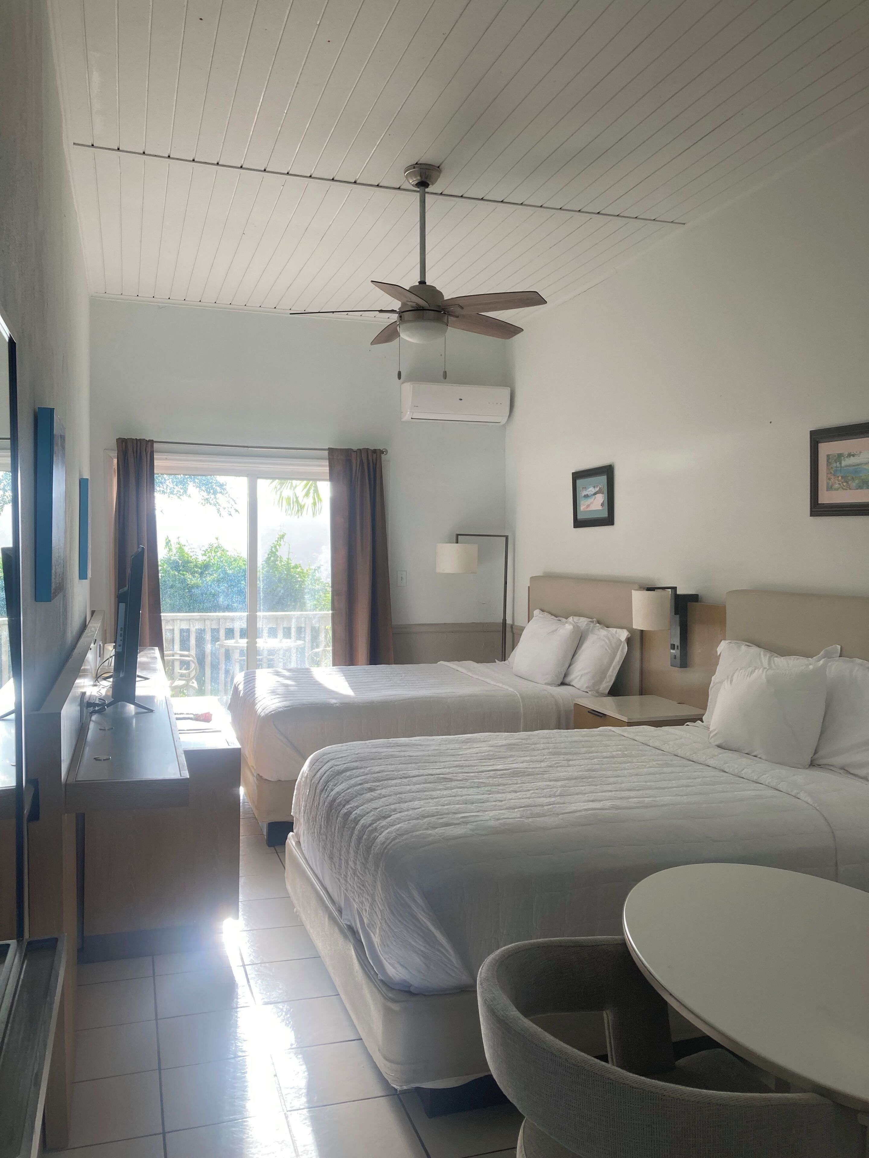 A hotel room with two beds, a desk, a chair, a ceiling fan, and a window with curtains.