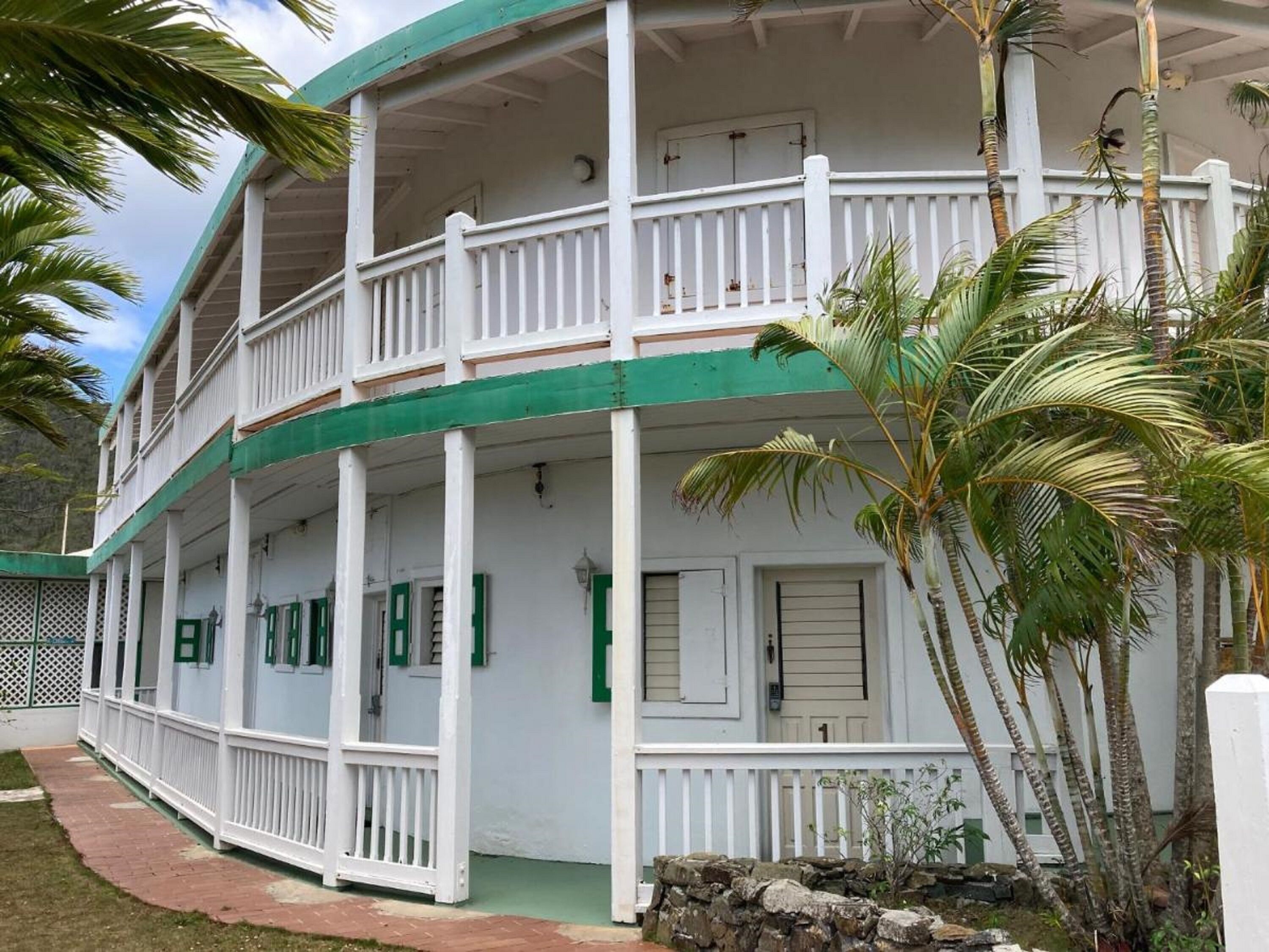 A two-story building with a balcony, white exterior, and green trim.