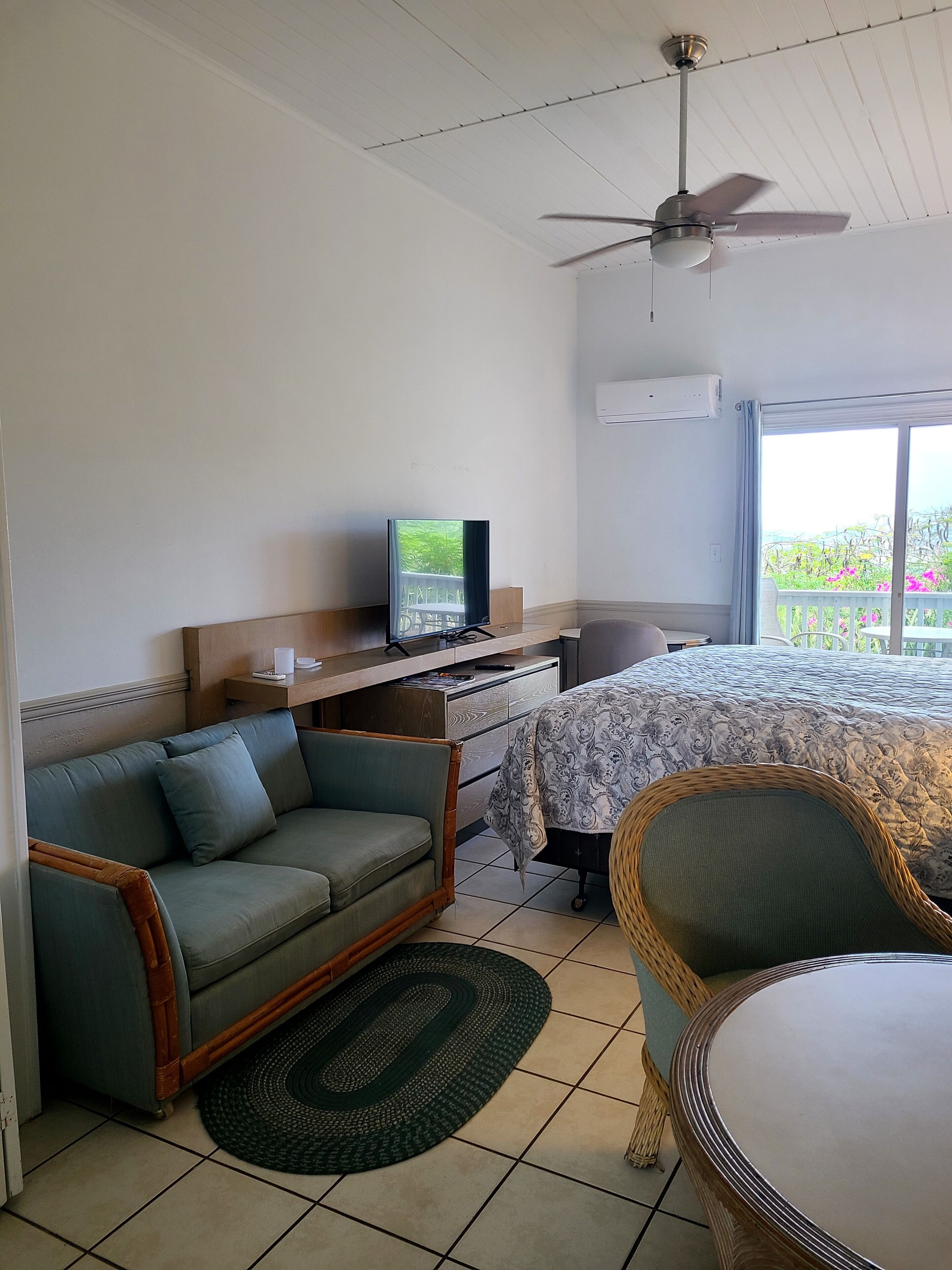 A hotel room with a bed, a sofa, a chair, a television, and a ceiling fan.