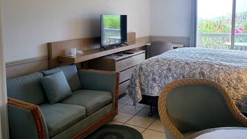 A hotel room with a bed, a sofa, a chair, a television, and a ceiling fan.