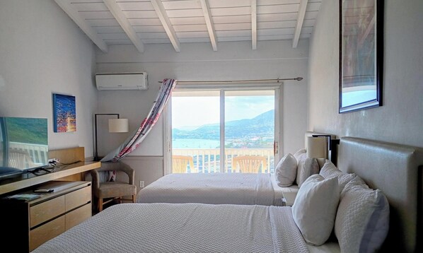 Ein Schlafzimmer mit zwei Betten, einem Schreibtisch, einem Stuhl und einem Fenster mit Blick auf eine Landschaft.