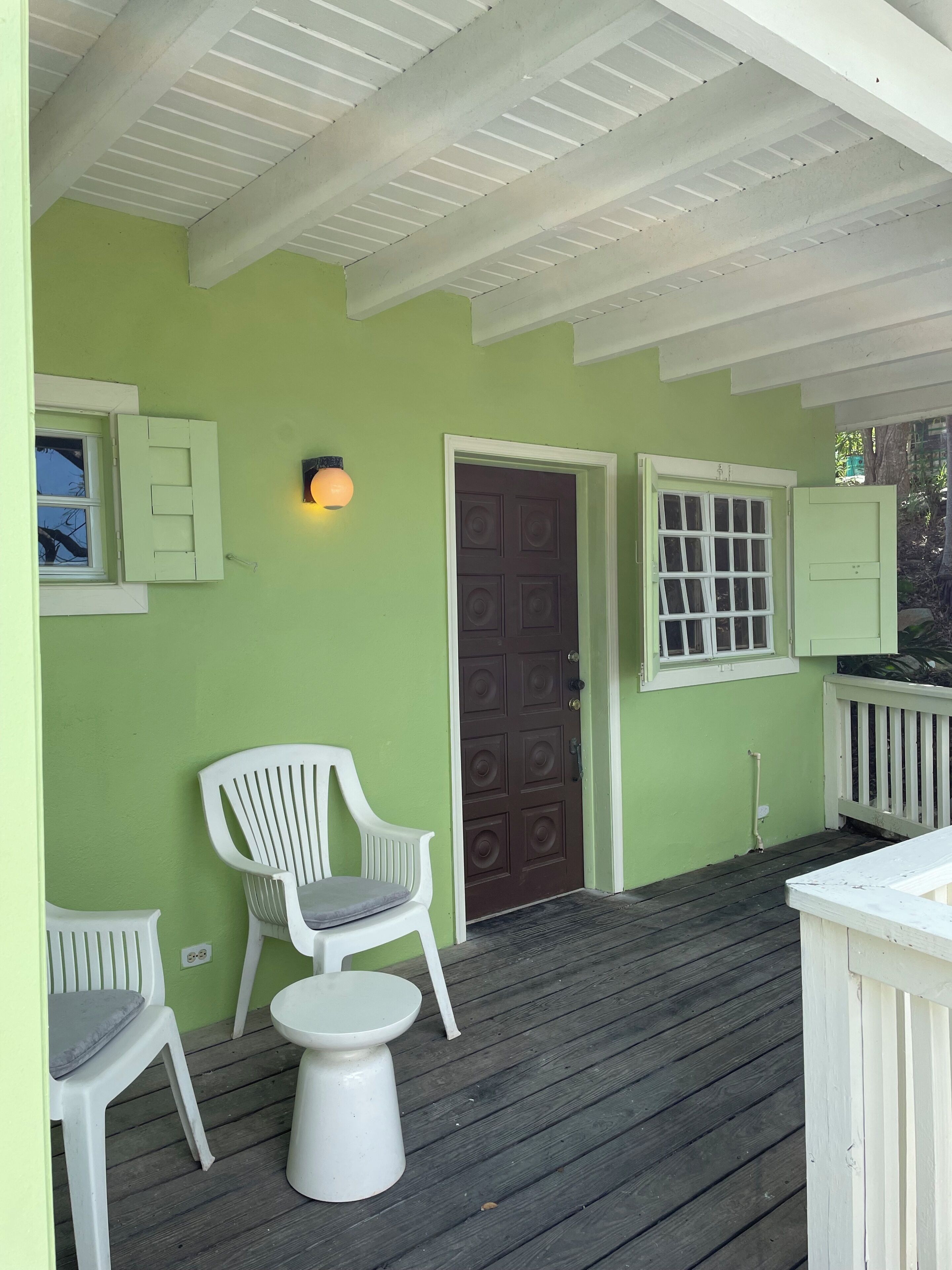 Een veranda met een groene wand, een bruine deur en twee witte stoelen.
