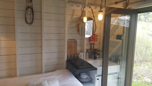 A room with a bed, a small kitchenette, a mirror, and a window with a view of greenery. - Laggan Bothies (Spean Bridge)