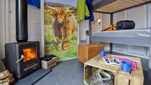 A cozy cabin interior with a wood-burning stove, a bunk bed, and a rustic wooden table with various items. - Laggan Bothies (Spean Bridge)