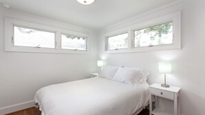Een slaapkamer met een bed, twee nachtkastjes en drie ramen.