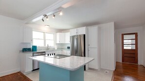 Een moderne keuken met witte kasten, een blauw eiland, roestvrijstalen apparatuur en een houten vloer.