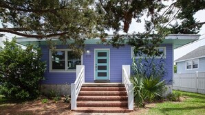 Een huis met een blauwe gevel, een veranda met witte leuningen en een voordeur met een groene deurbel.