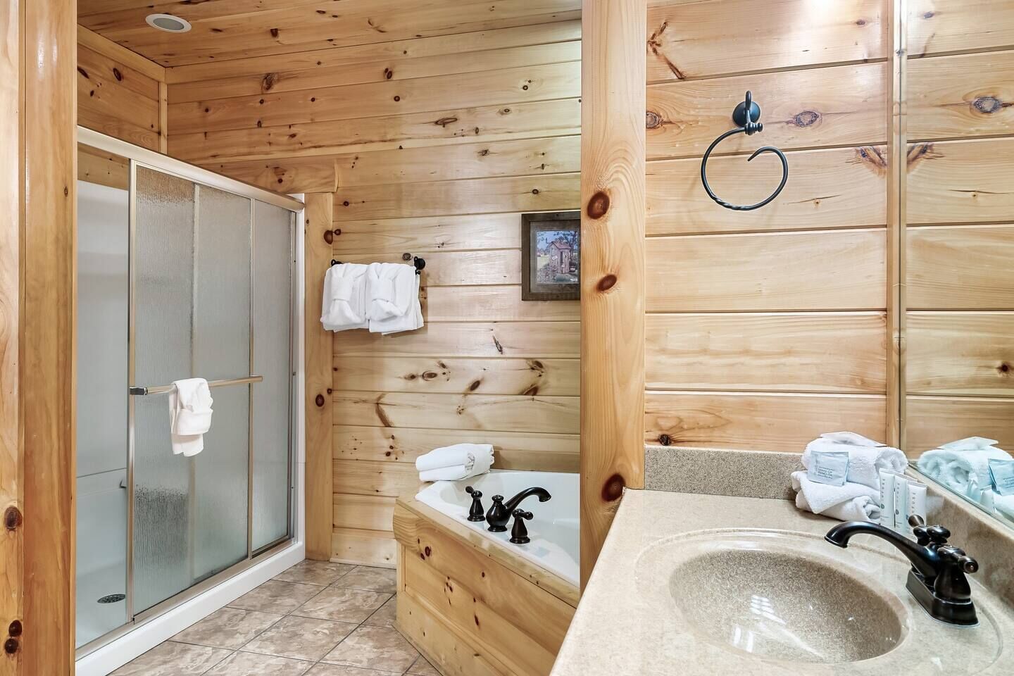 Un baño de cabaña de madera con mampara de vidrio, un lavamanos con espejo y toallas colgadas en un perchero.